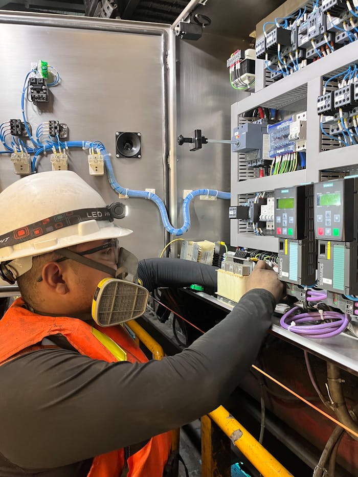 who-we-are Electrician wearing safety gear adjusting wires on a control panel in Callao, Perú.