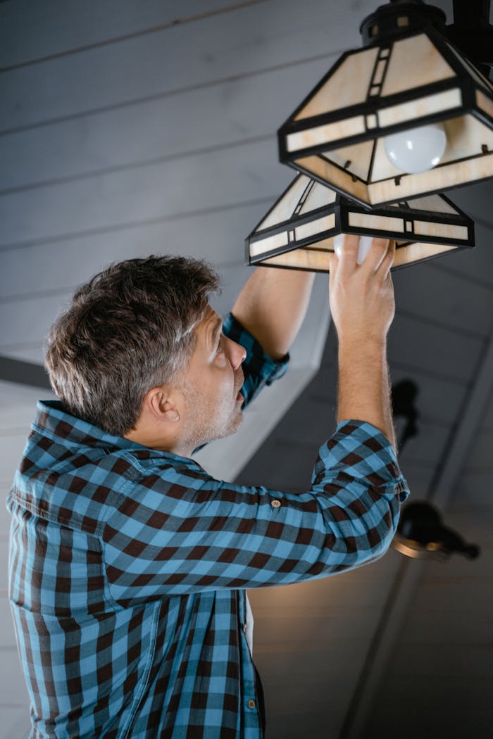 journey Adult male fixing pendant light indoors, wearing plaid long sleeves. Home maintenance scene.